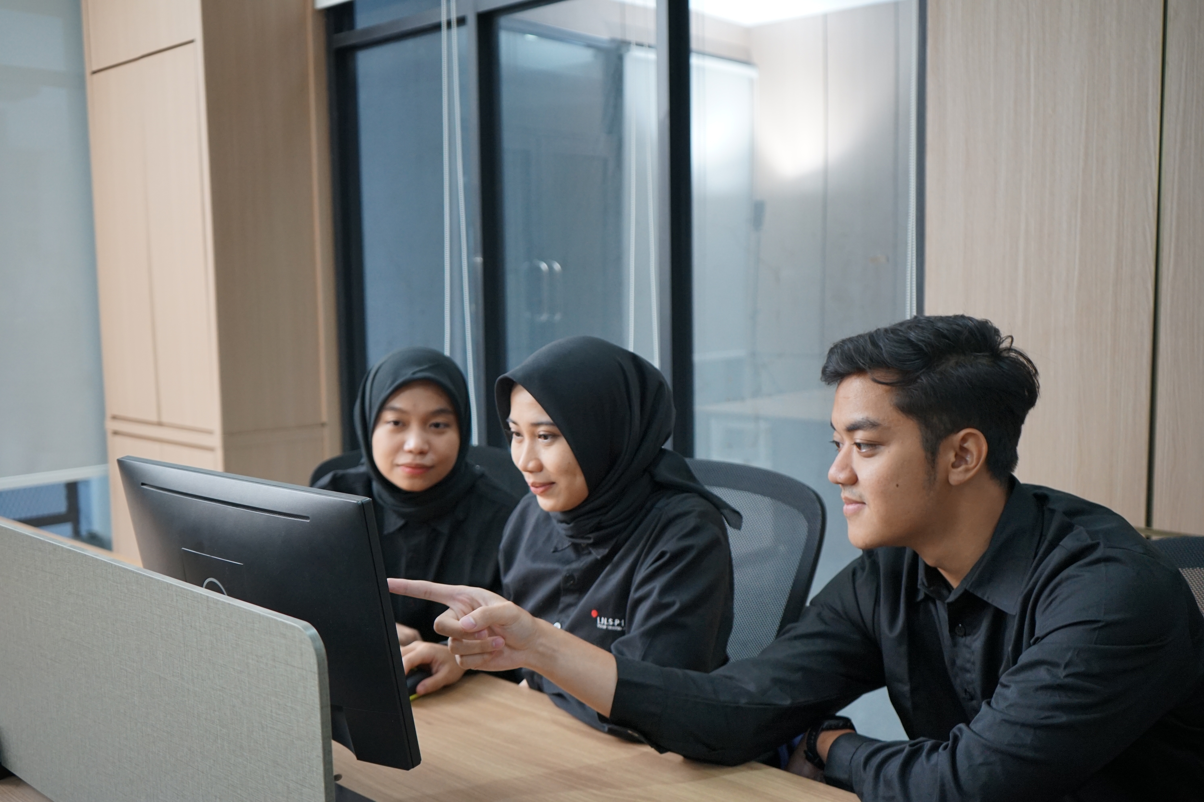 three people watching and pointing at a monitor